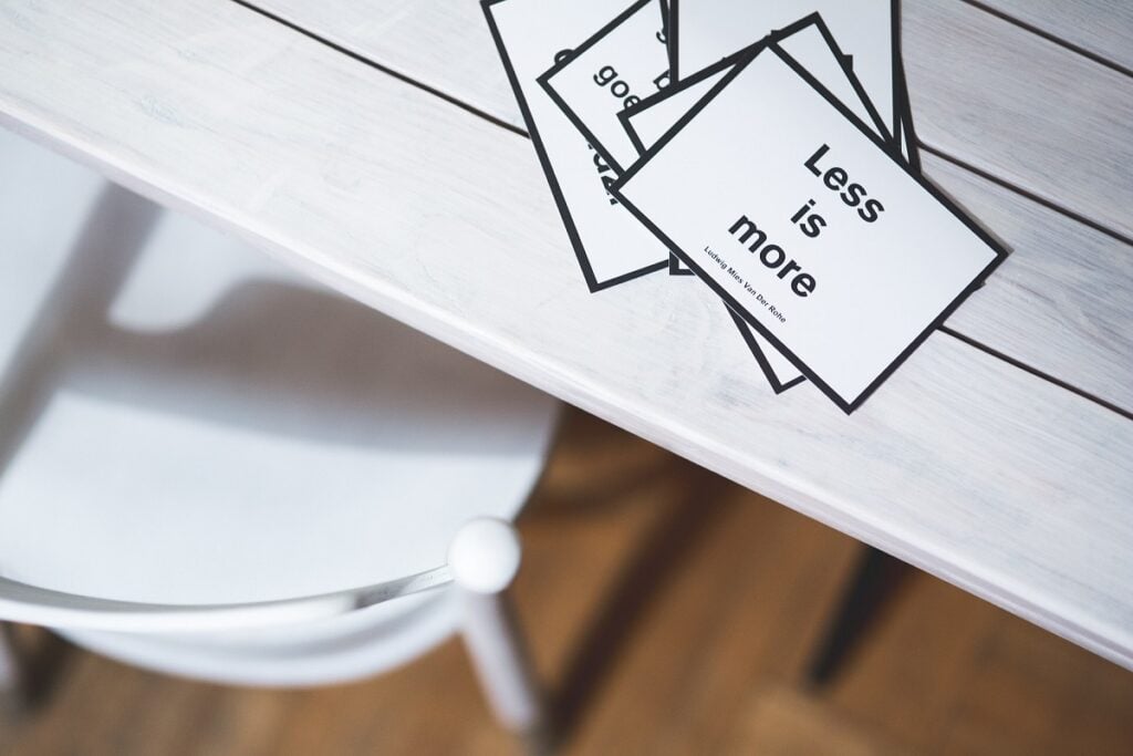 A small card with black letters on a white background, on a white table. The card says "Less is more".