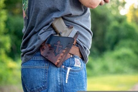 Will There Be Guns In Heaven? A man's waist, with a holster and gun on his belt, and a cross on the holster.
